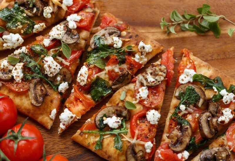 A wooden table or tray with sliced up flatbread pizza, which contains feta and spinach