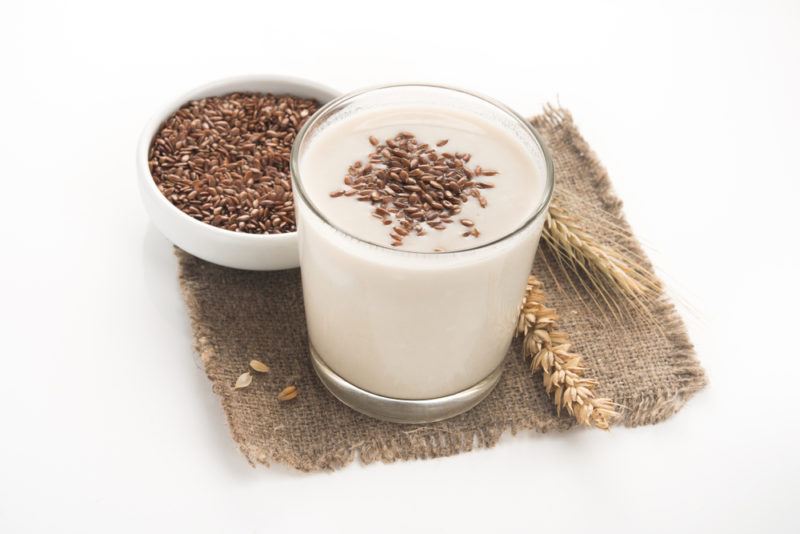 A glass of flax milk next to a white bowl of flaxseeds