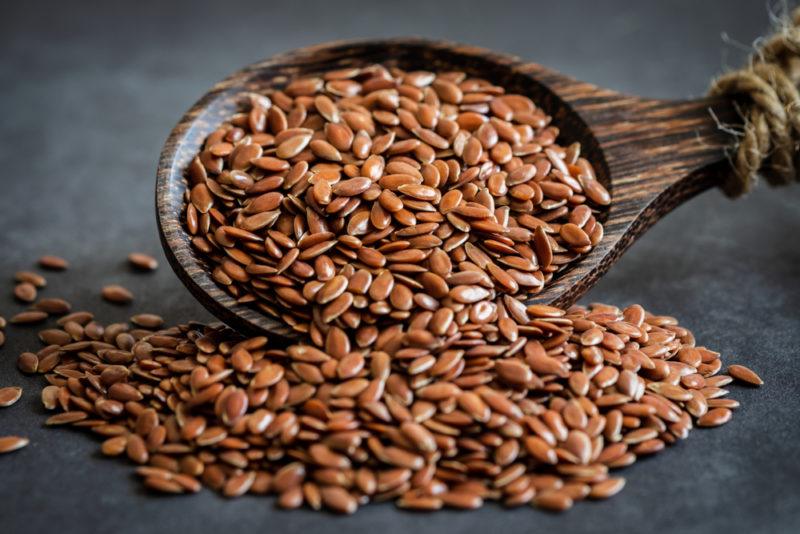 A large spoon of flax seeds where some of the flax seeds are being poured out onto the table