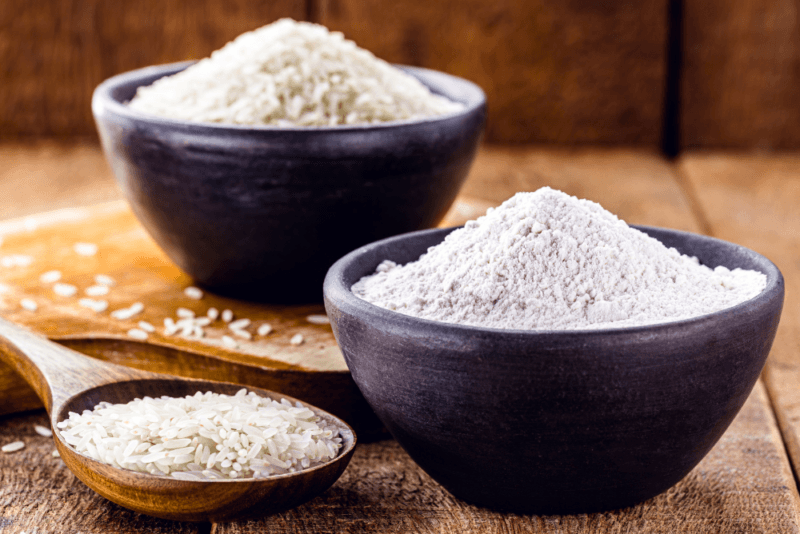 A black bowl and a wooden spoon containing rice, plus another black bowl with rice flour