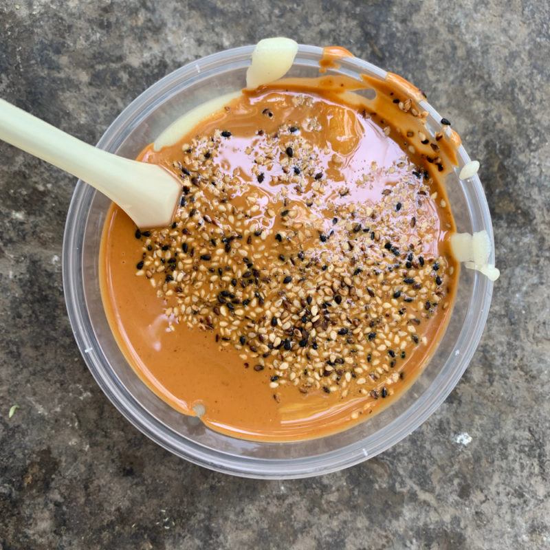 A clear container of flour tea with sesame seeds and a straw or chopstick