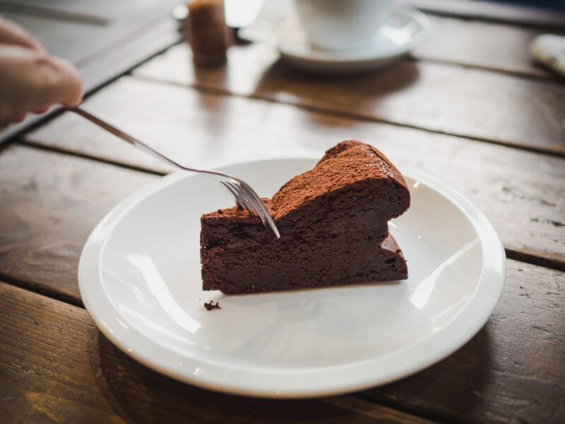 on a wooden table is a round ceramic dish with a slice of flourless cake with a hand shoving a fork in it