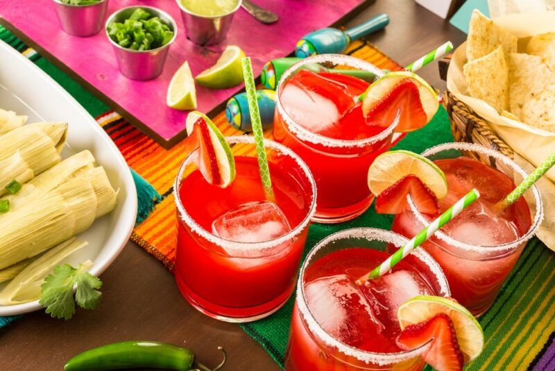 Four glasses of a Hot Tamale Fireball cocktail on a table with a variety of Mexican foods