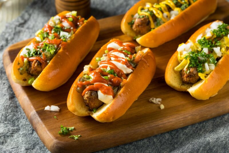 Four freshly made hot dogs on a board, each with a plant-based sausage and plenty of appetizers