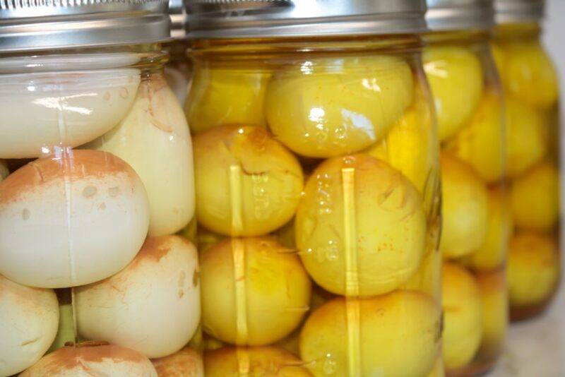 Four jars of pickled eggs, where the liquid in one jar is mostly clear, while it is yellow in the other jars instead.