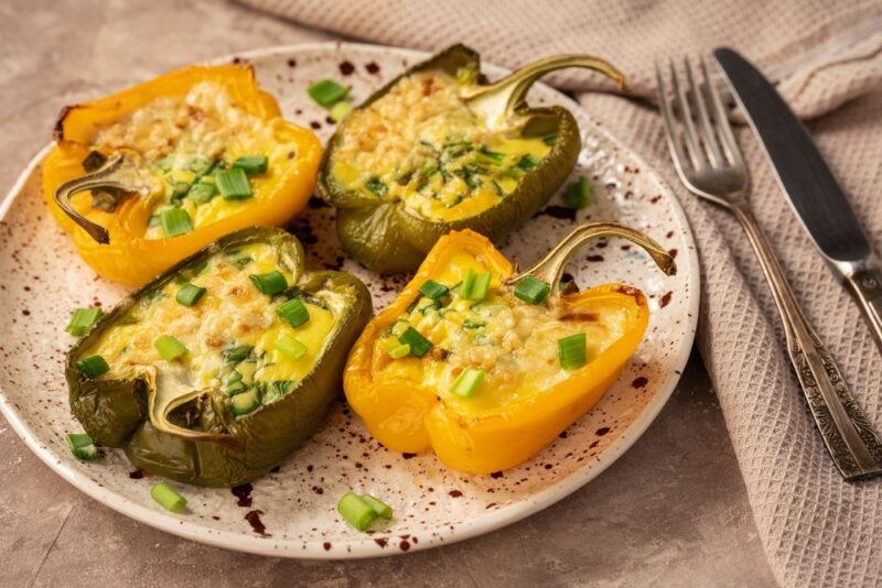 A speckled plate with two green and two yellow pepper halves, each stuffed with egg, cheese, and bacon