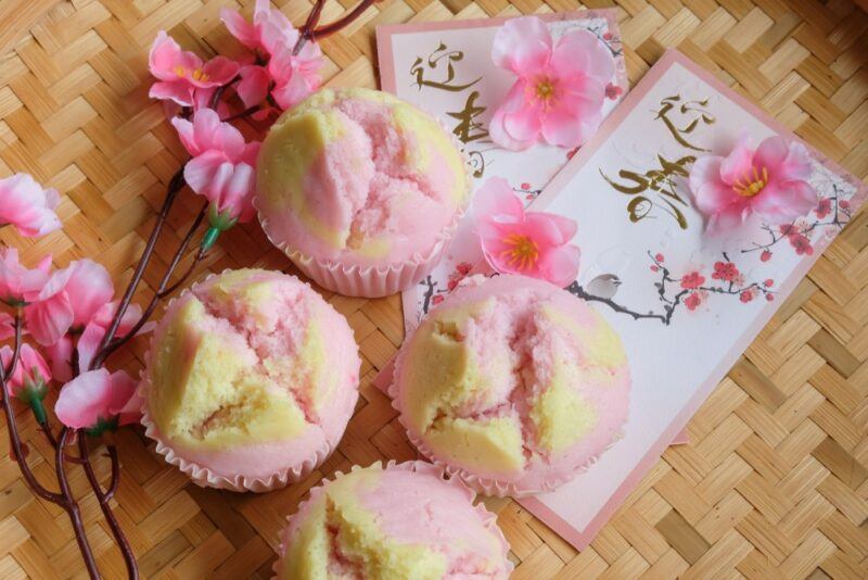 A wooden table with four pink and yellow Chinese fortune cakes, plus pink blossoms and cards with illustrations