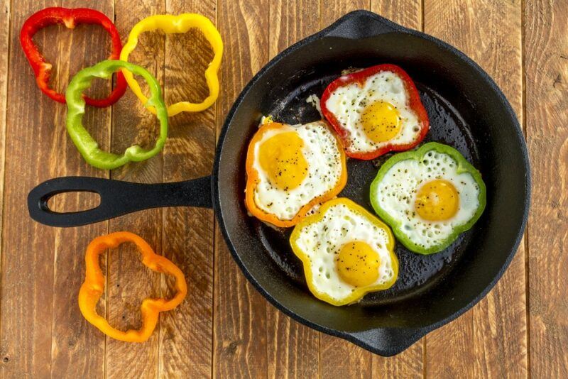 A black cast iron frypan will four bell pepper fried eggs and some bell pepper slices on the side