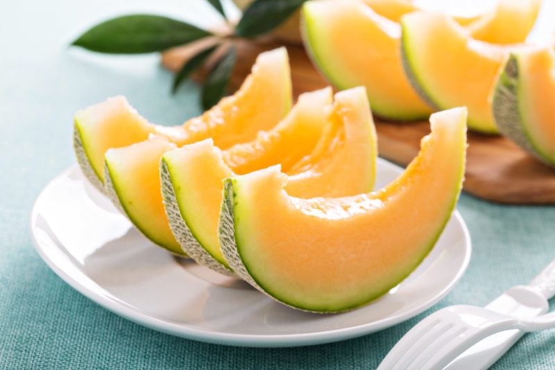 Sliced cantaloupes with their skins on, lined up on a round white plate