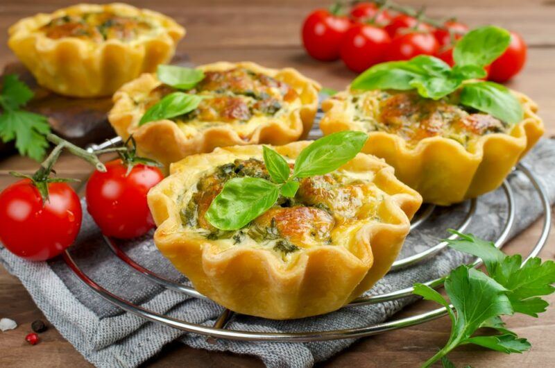 A metal cooling tray containing four small quiches, with some cherry tomatoes as well