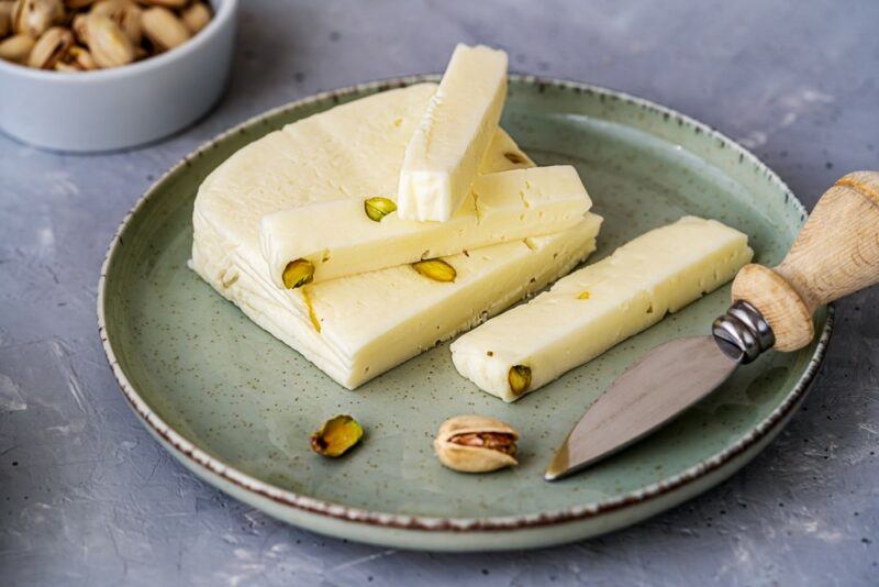 A gray plate with pieces of asiago cheese that includes some pistachio nuts inside