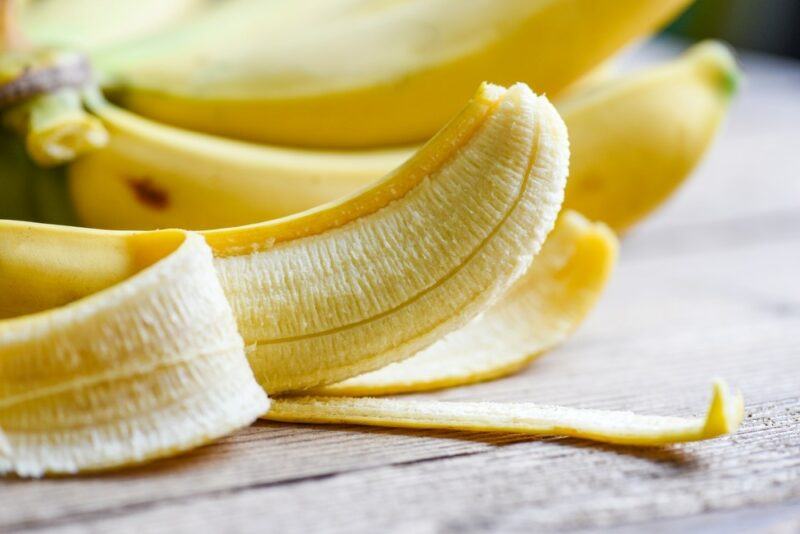 Fresh bananas on a table, one of which has been peeled