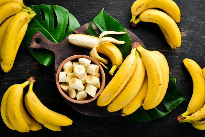 Fresh bananas in bunches on a table, with a wooden bowl of sliced bananas