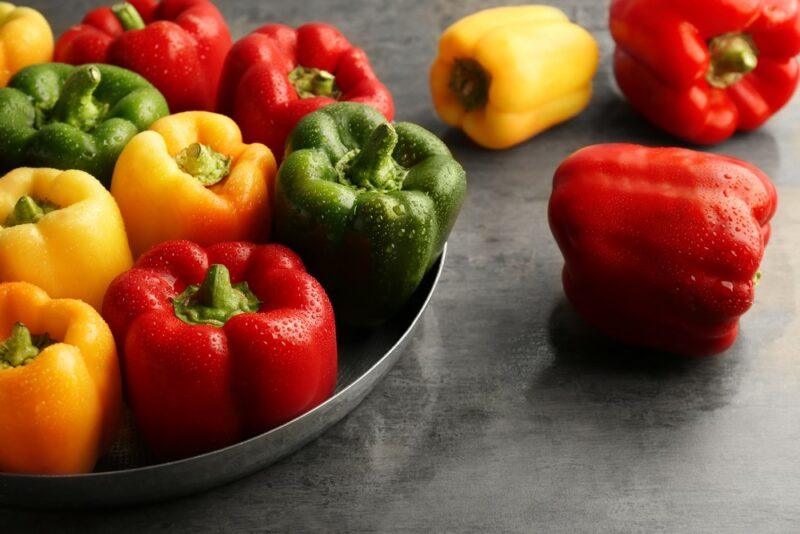 A metal tray of fresh bell peppers, including yellow, green, and red ones