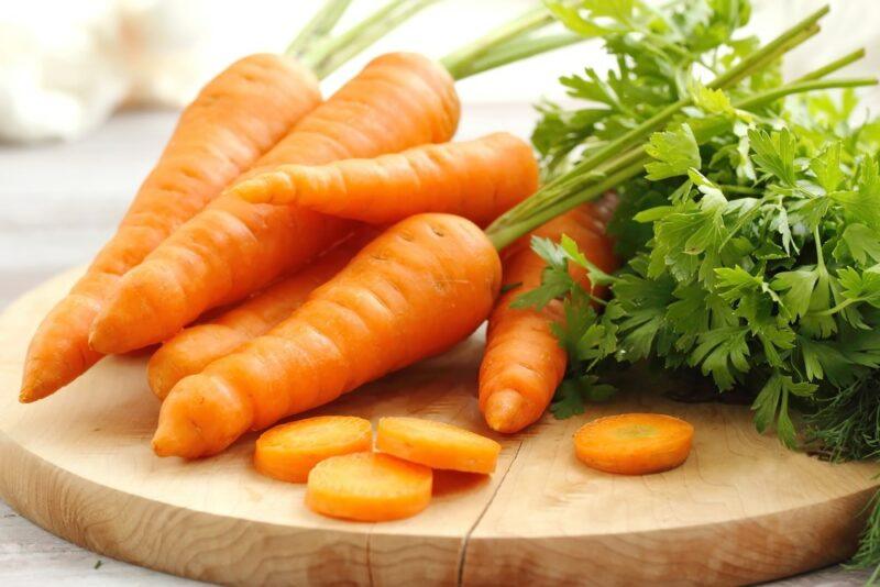 A circular wooden board with fresh carrots and a few carrot slices