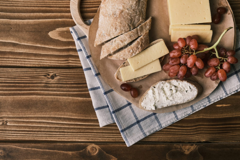 Sliced fresh ciabatta with cheese and grapes on a wooden board and a tea towel