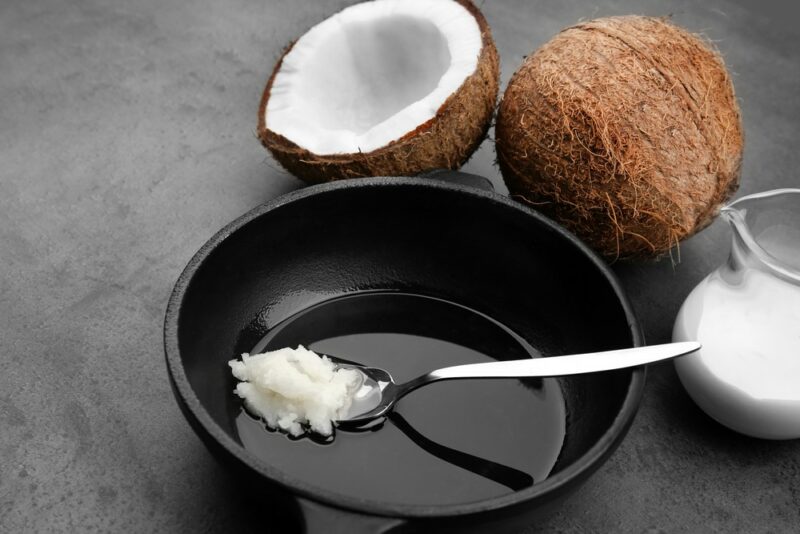 A black dish with a spoon of coconut oil, surrounded by a full coconut, half a coconut, and some coconut oil