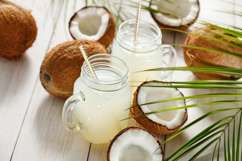 Two mason jars of coconut water and various fresh coconuts and coconut halves scattered across the table