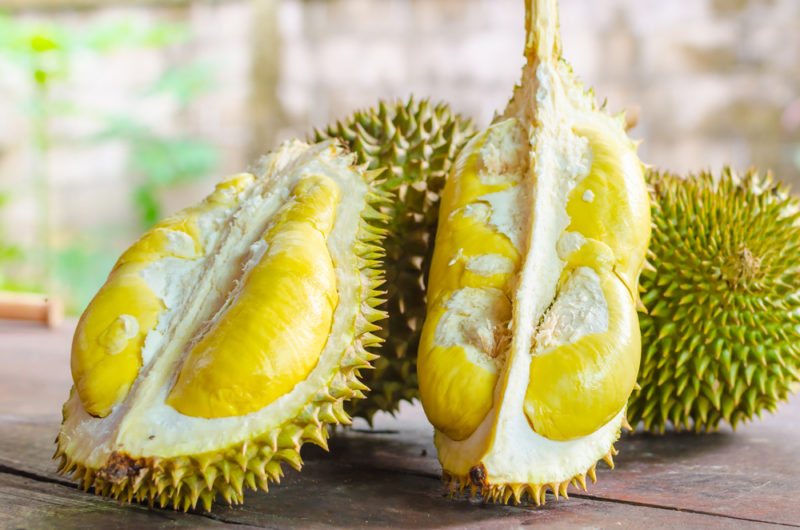 Two full durian fruit and one that has been cut in half so that the inside can be seen