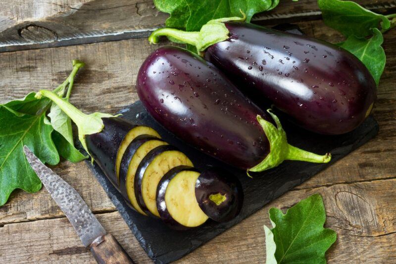 A wooden table with a black slate containing two eggplants and some sliced eggplants