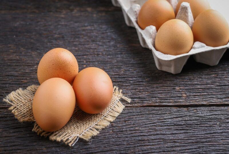 A dark table with eggs in a carton and three eggs on a cloth