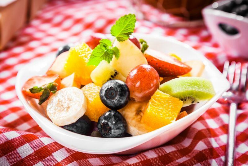 A red and white checkered picnic blanket, with a small white plate of fruit salad