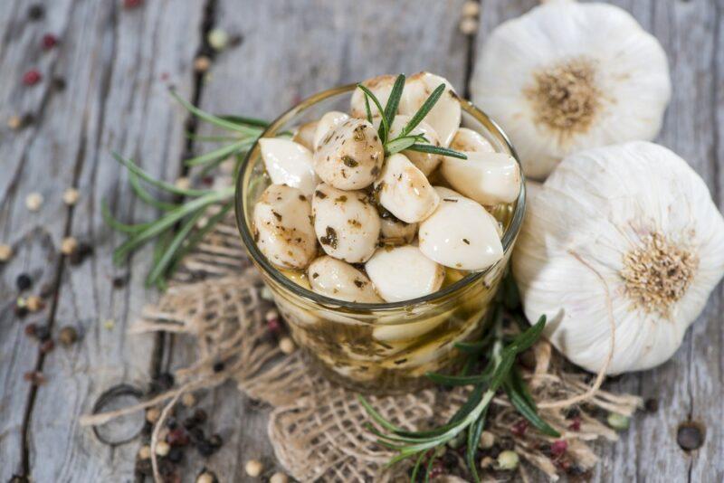 A glass jar of fermented garlic cloves, next to some pieces of garlic on a wooden table