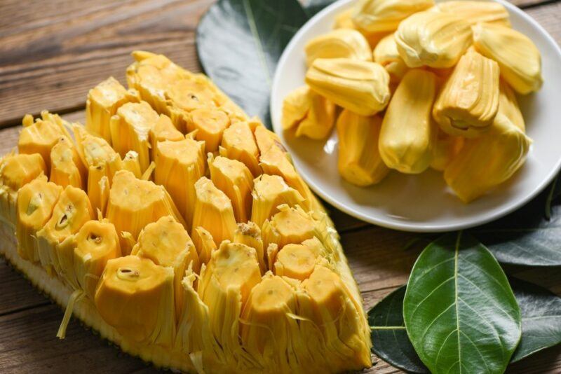 Half a jackfruit with the flesh still attached, plus a small white plate with more pieces of jackfruit flesh