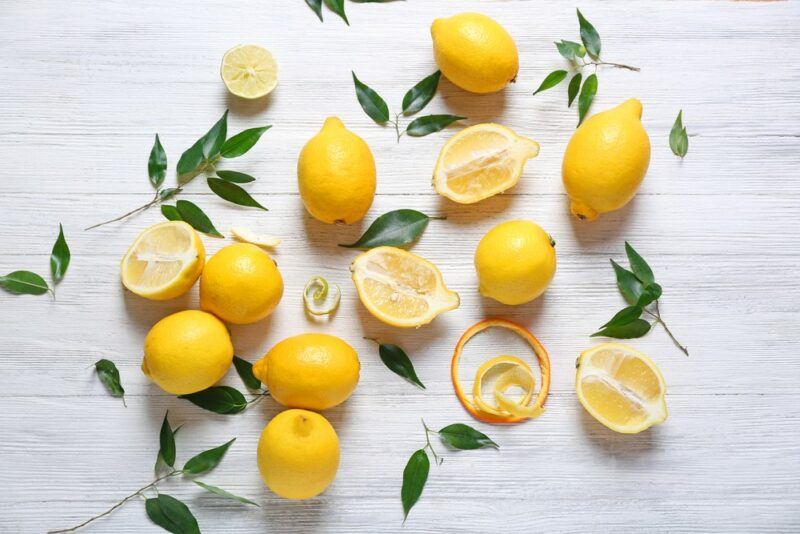 A white table with fresh lemons and lemon halves, along with leaves