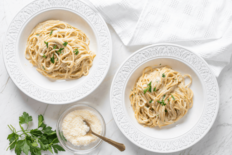 Two white bowls containing fresh pasta with parmesan, next to a glass bowl of parmesan cheese