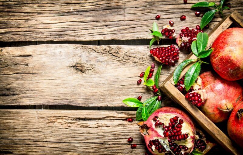 A wooden table with some fresh pomegranates and a box