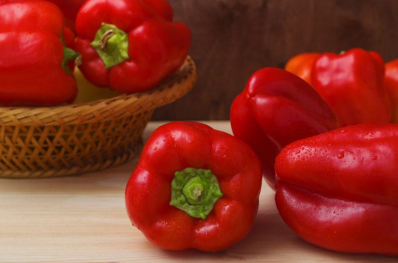 A selection of fresh red bell peppers, some on a table others in a basket