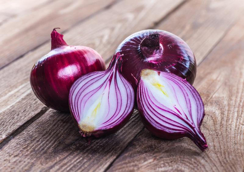 Three fresh red onions on a wooden deck, one of which has been cut in half