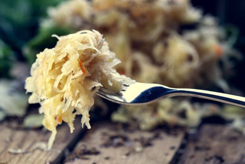 A single fork with sauerkraut being held up to the camera. Everything in the background is out of focus and cannot be easily identified.