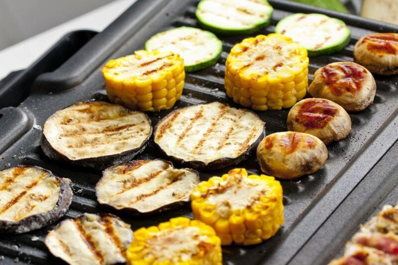 A close up image of a black smokeless frypan with grilled vegetables, including zucchini and corn