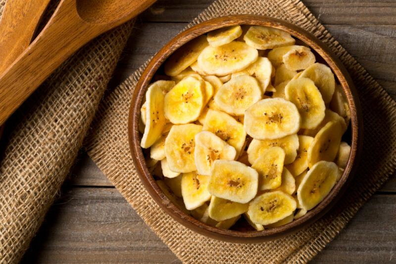 A wooden bowl with banana chips next to spoons