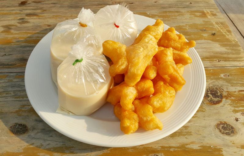 A white plate with deep fried dough sticks and soy milk in bags