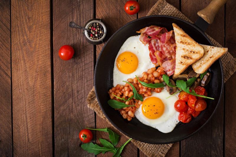 A black fry pan with eggs, bacon, beans, and toast