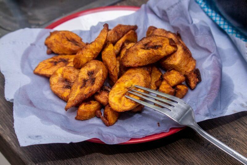 A red and white plate with a piece of paper and fried maduros