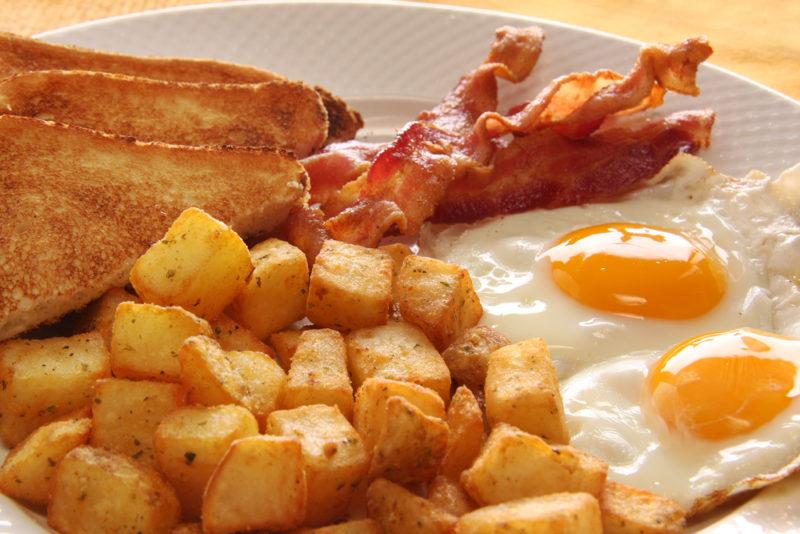 A cooked breakfast with fried potatoes, bacon and eggs