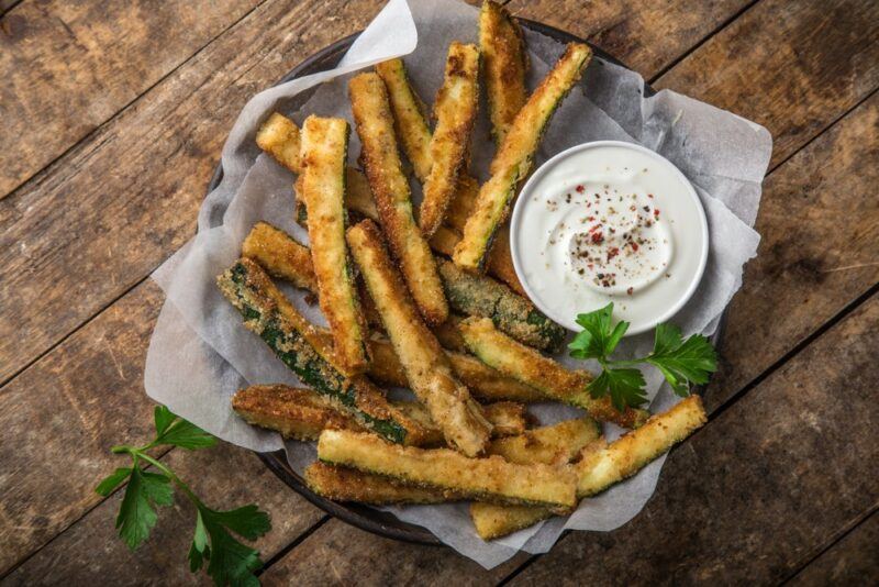 A dish of fried zucchini chips next to some dip