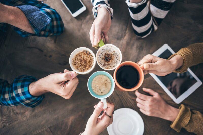 A pair of four friends clinking coffee mugs together