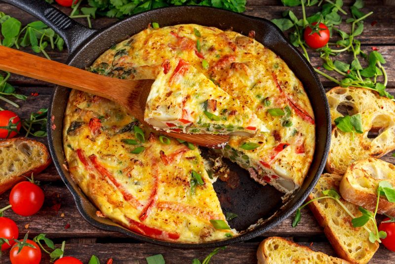 A frittata in a large cast iron frypan with a wedge cut out and placed on a wooden spoon