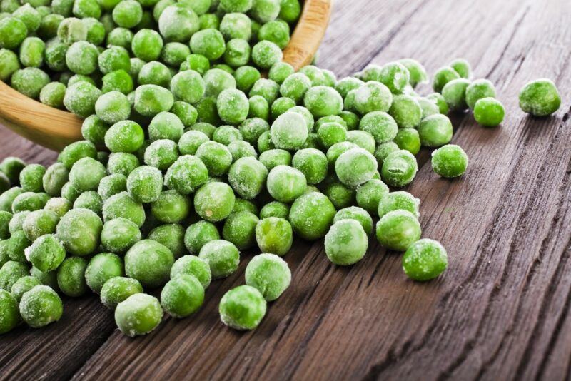 A dish of frozen peas that's spilling out onto the table