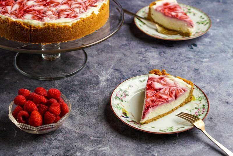 A frozen raspberry lemonade pie on a cake stand, with two pieces on small plates