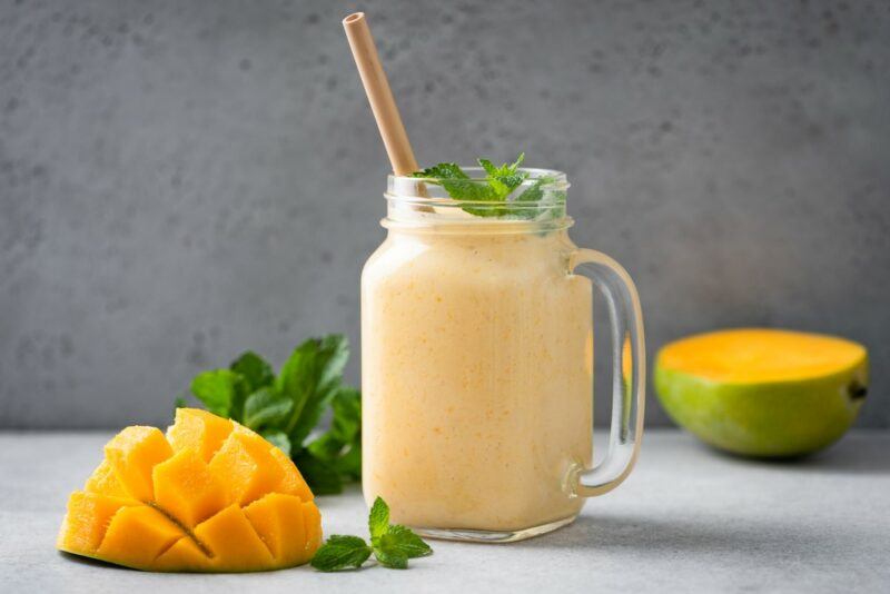 A smoothie like frozen spiced rum mango lassi cocktail in a mason jar, next to some mango halves