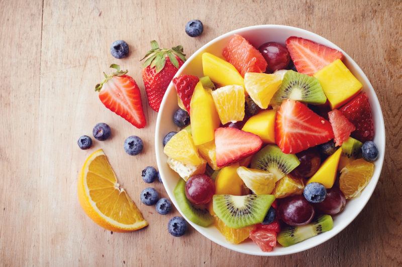 A bowl of fresh fruit in a bowl on a wooden table