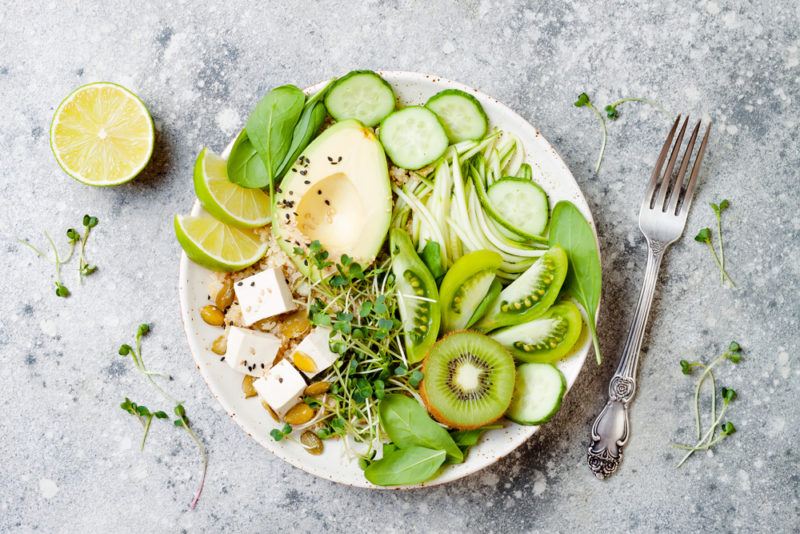 A white protein bowl with kiwis and other greens