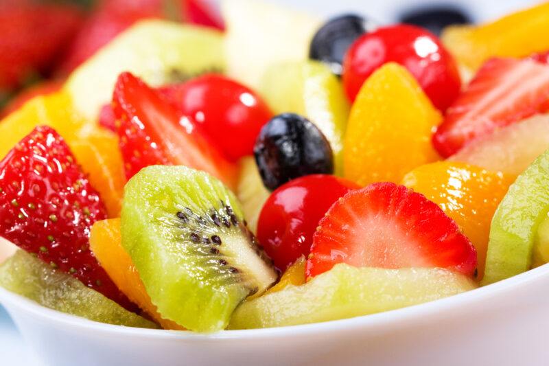 This photo shows a closeup of a variety of cut fruit in a white bowl.