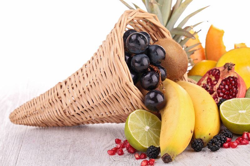 variety of fruit spilling out of cone shaped basket like grapes, kiwi, bananas, lime, and pomegranate